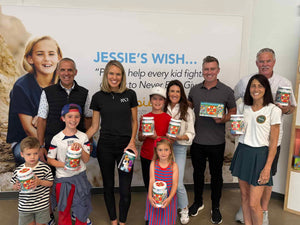 Group of people holding containers with a 'Jessie's Wish' poster in the background